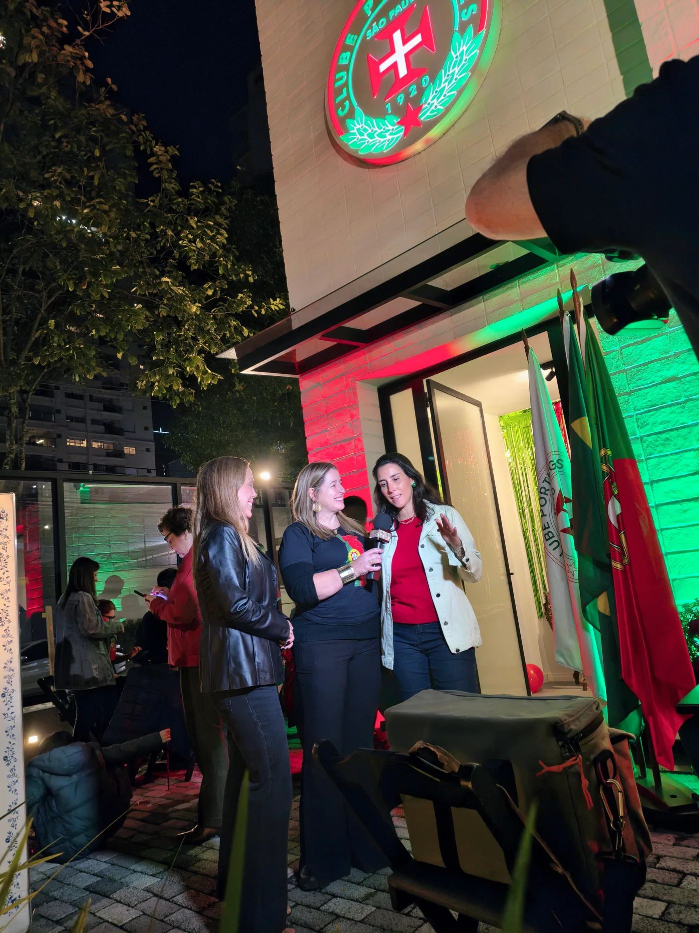 Convidadas reunidas junto à entrada iluminada da sede